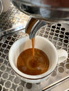 Espresso läuft aus dem Siebträger in eine weiße Tasse auf dem Abtropfgitter einer Siebträgermaschine