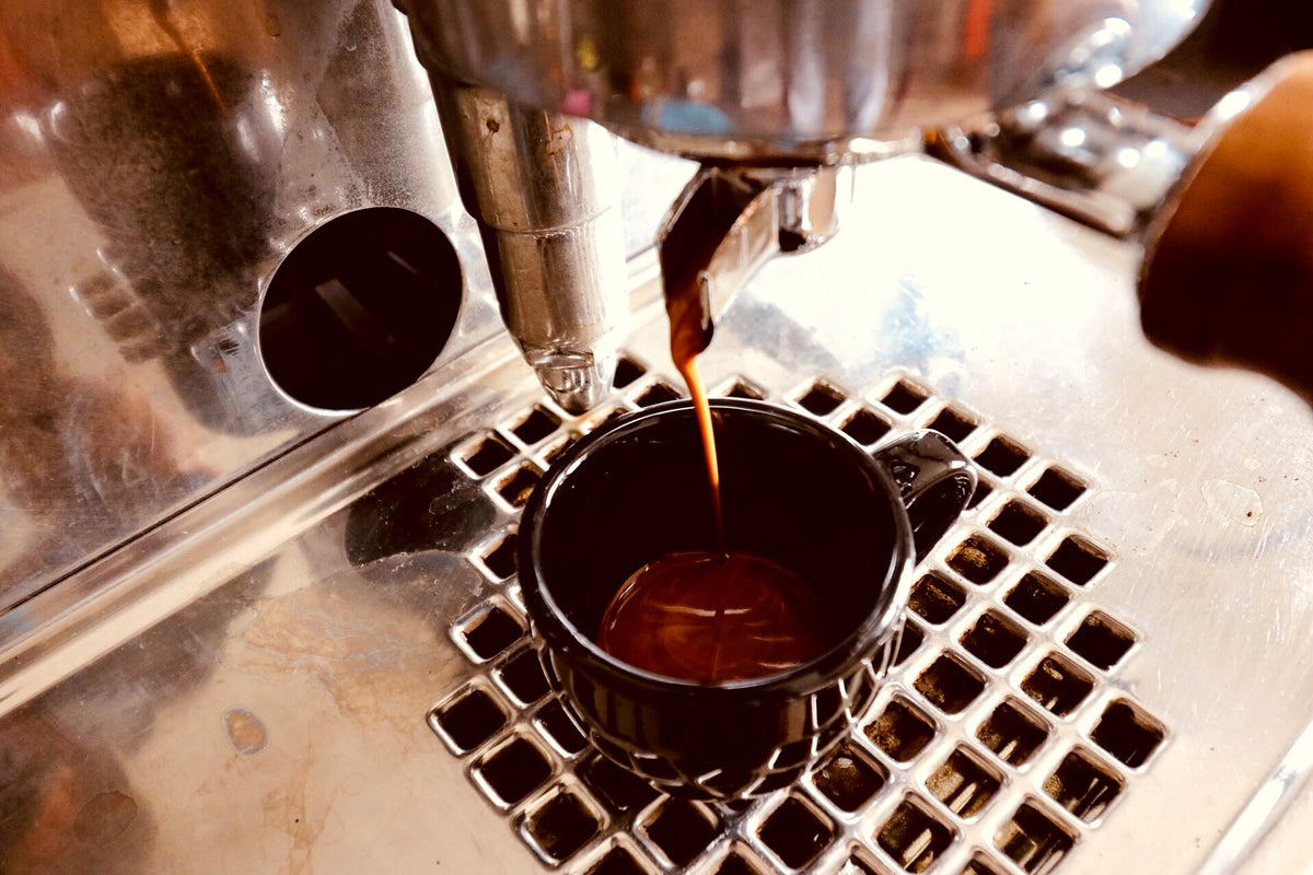 Espresso läuft in schwarze Tasse, warmer Look